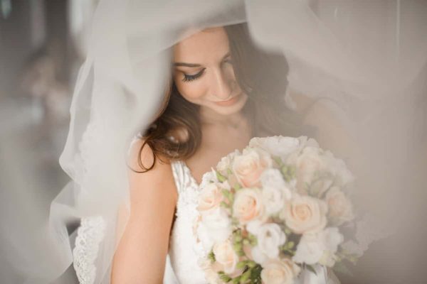 Bride morning preparation. Lovely and young bride in a white veil holding a beautiful wedding bouquet of flowers